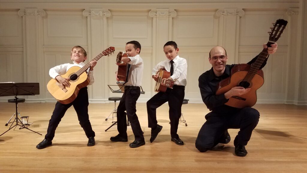 Three young boys and their teacher pose in fun positions with their classical guitars.
